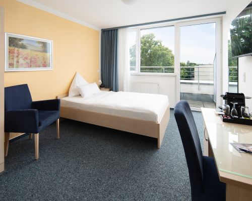 Einzelzimmer mit Bett, Balkon, TV und Schreibtisch.