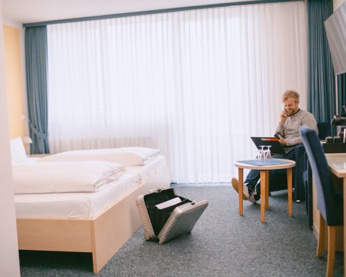 Doppelzimmer mit Balkon, Bett, Schreibtisch, TV und Sitzbereich.