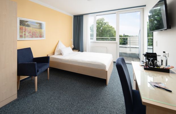 Helles Einzelzimmer mit Balkon, Bett und Sitzbereich.