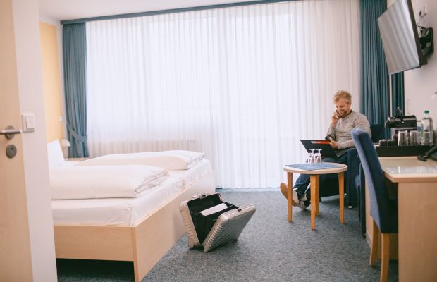 Helles Doppelzimmer mit Balkon, Bett, Schreibtisch, TV und Sitzbereich.