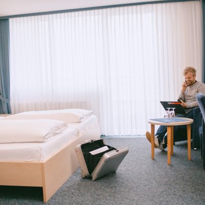 Helles Doppelzimmer mit Balkon, Bett, Schreibtisch, TV und Sitzbereich.