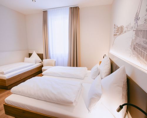 Standard-Dreibettzimmer mit mehreren Schlafplätzen, Sessel und hellem Fensterbereich.