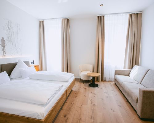 Doppelzimmer im Johanniter Gästehaus Münster mit Doppelbett, Sofa und großen Fenstern.