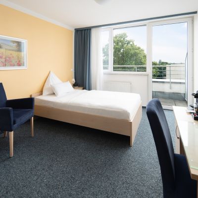 Helles Einzelzimmer mit Balkon, Bett und Sitzbereich.