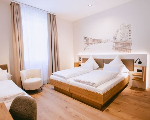 Modernes Standard-Dreibettzimmer mit Doppelbett, zusätzlichem Bett, Holzboden und großem Fenster.