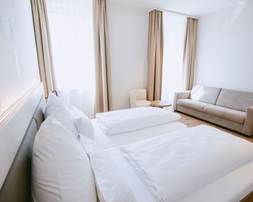 Standard Doppelzimmer für 4 Personen mit Doppelbett, Sofa, kleinem Tisch und viel Tageslicht.