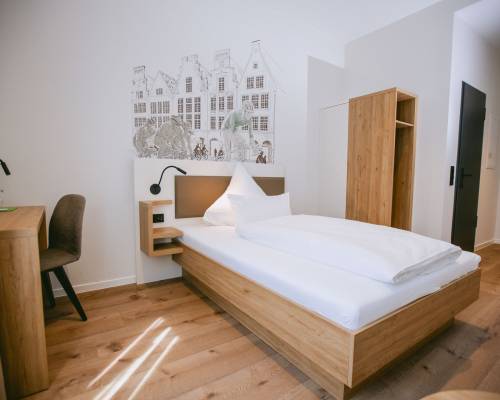 Modernes Standard Einzelzimmer mit Einzelbett, Holzmöbeln und Wandgestaltung im Johanniter Gästehaus Münster